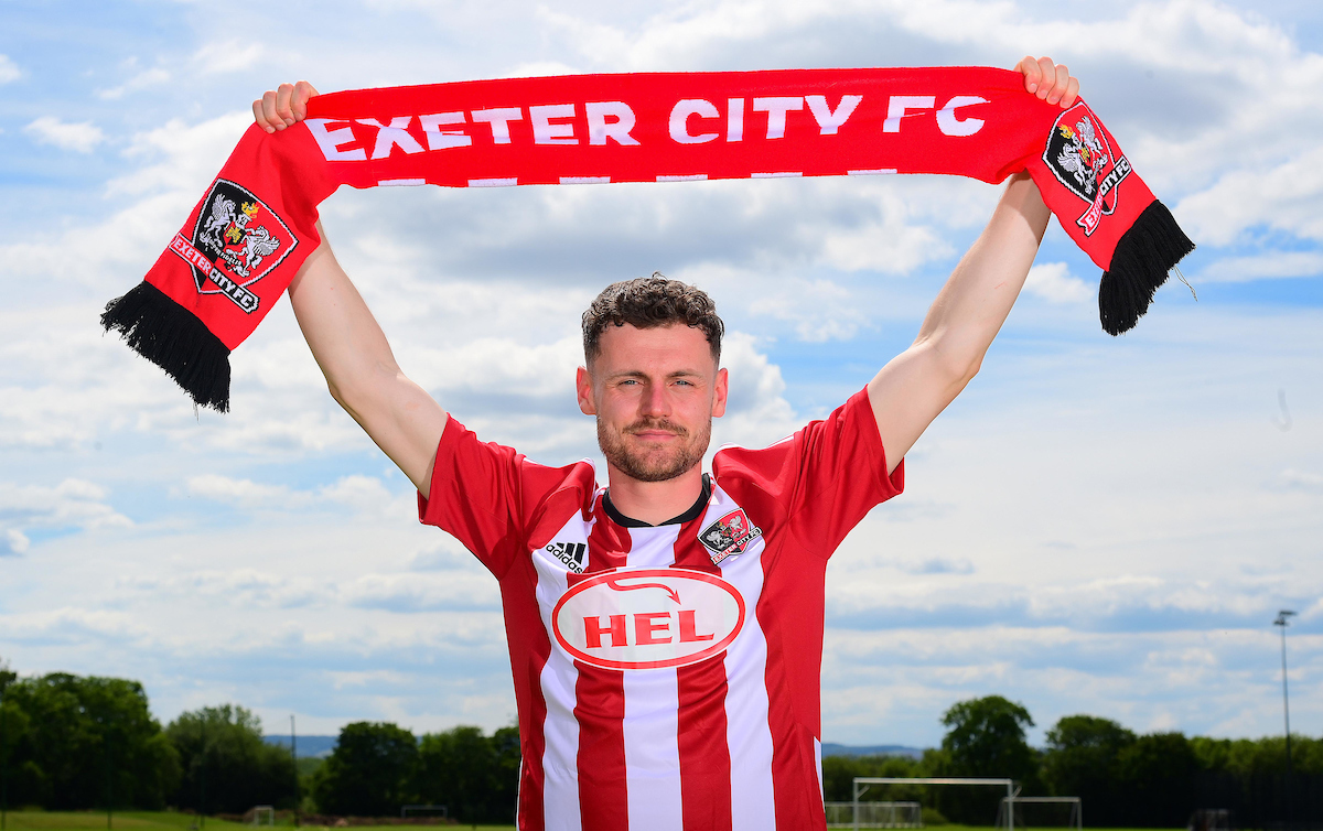 Jack McMillan holding aloft a scarf which says Exeter City FC