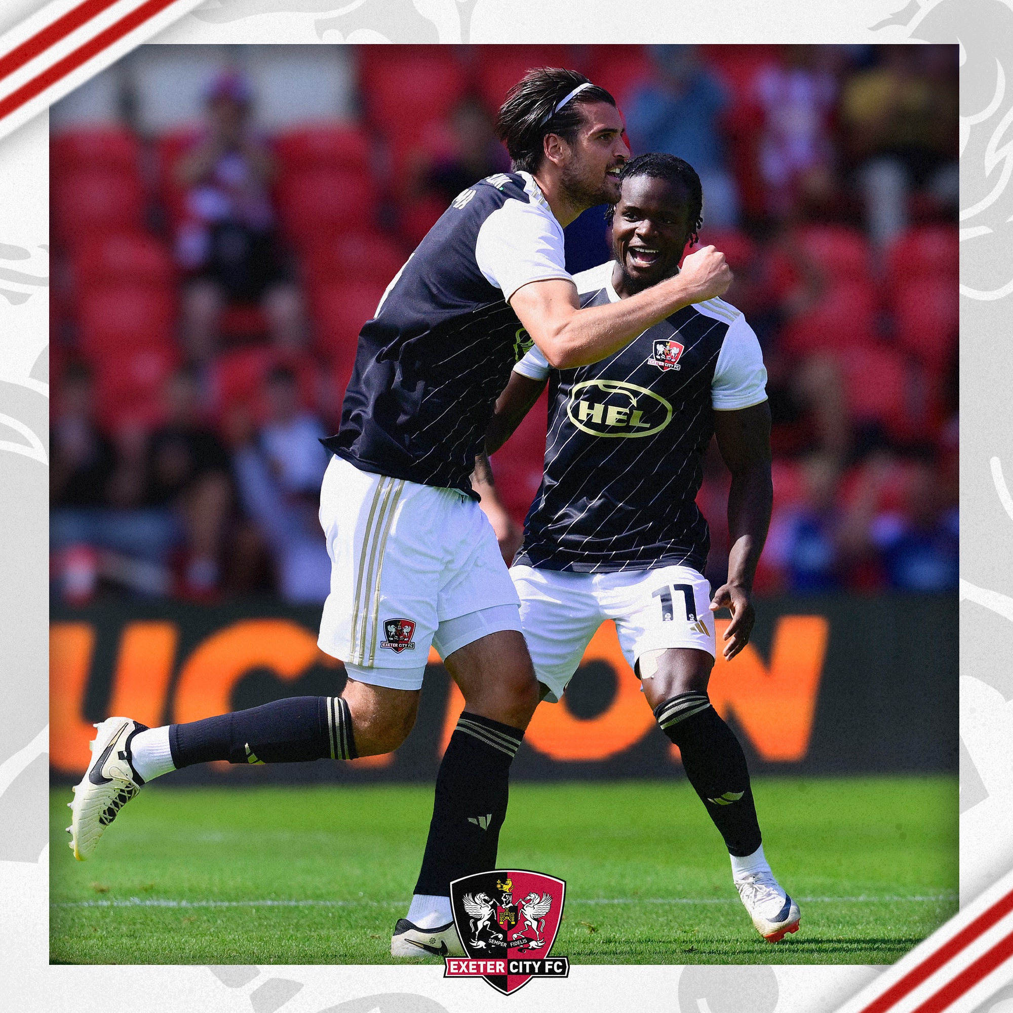 City player Tristan Crama celebrating the opener. He's wearing a black top with white shoulders, white shorts and black socks and is making a fist as he runs to celebrate. Millenic Alli can also be seen celebrating in the background.