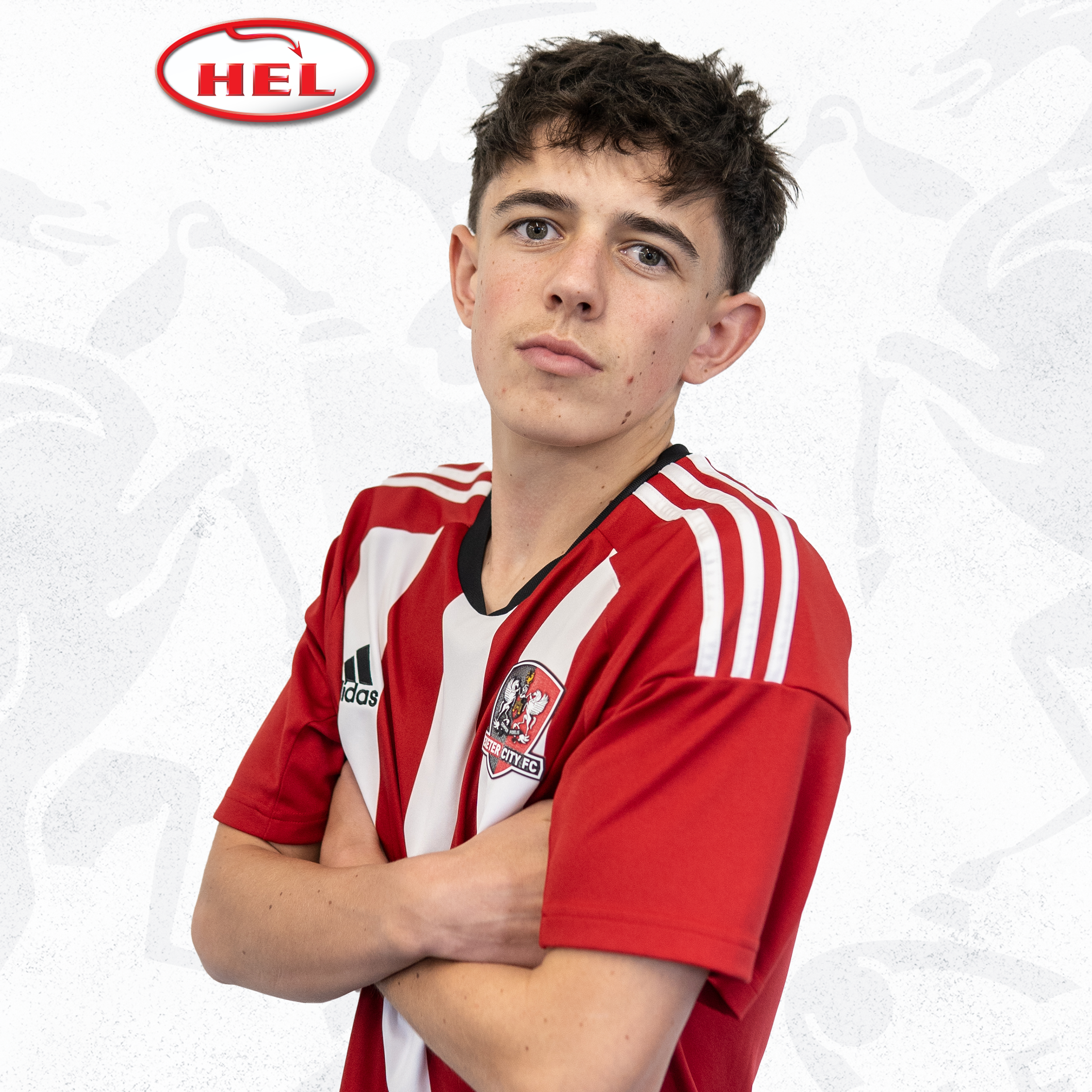 Under-18 player Aidan Bown standing with his arms folded, side on, looking at the camera. He's wearing the red and white home kit, and has a dark fringe. The HEL logo is in the corner.