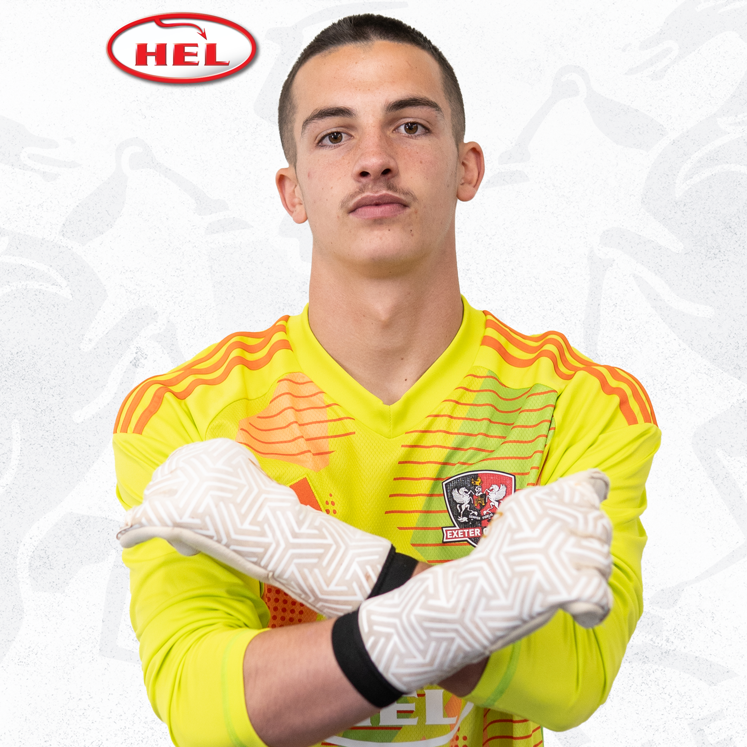 Under-18s player profile picture of Dylan Shanahan. He's wearing the bright yellow and orange goalkeeper shirt, and is holding his arms in an 'X' position, with his goalkeeper gloves on. He's got short dark hair and a light moustache.