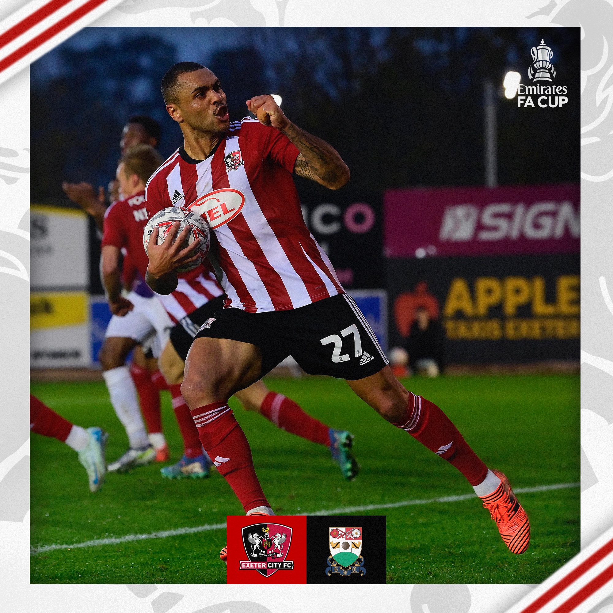 Josh Magennis, in his red and white home kit, celebrating his hat trick goal with a clenched fist towards the Big Bank while holding the ball.