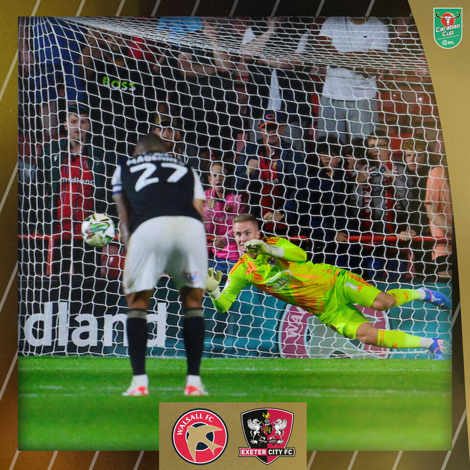 Joe Whitworth diving to save Walsall's penalty. You can also see the back of josh Magennis, who is bent over watching the penalty, and the ball in flight.