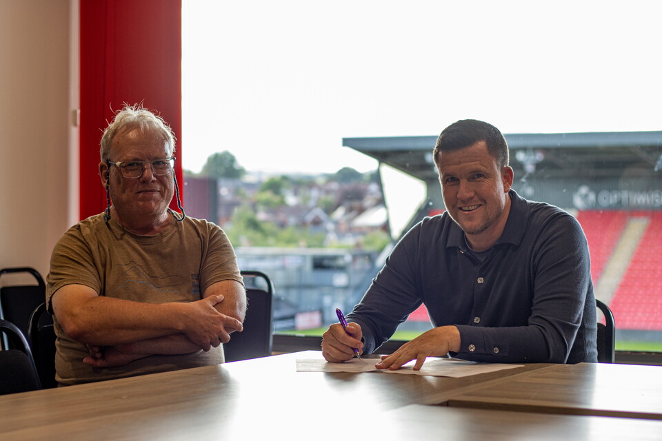 Image of Gary Caldwell signing his contract. On the right of the image is Gary signing the contract, on the left is Exeter City club chair Nick Hawker with his arms folded.