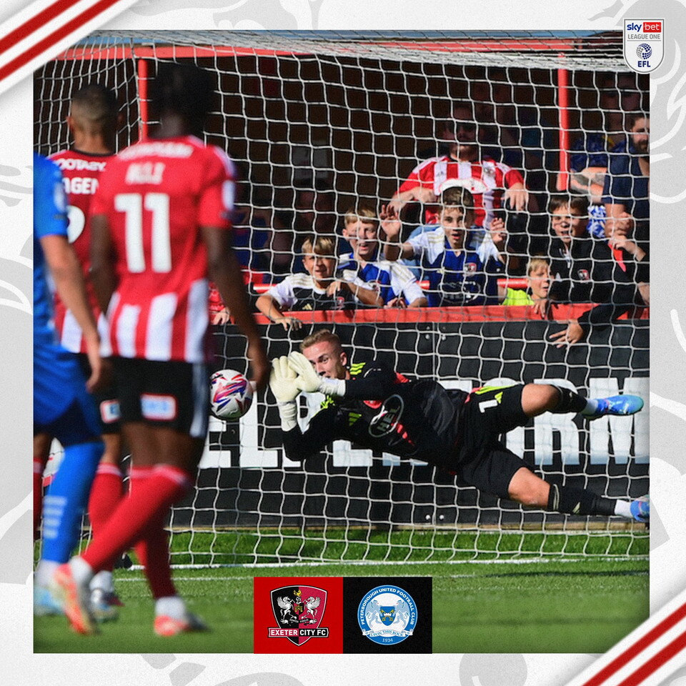 Image of Joe Whitworth saving the penalty, in a black kit he's diving to his right, palms out diving towards the ball.