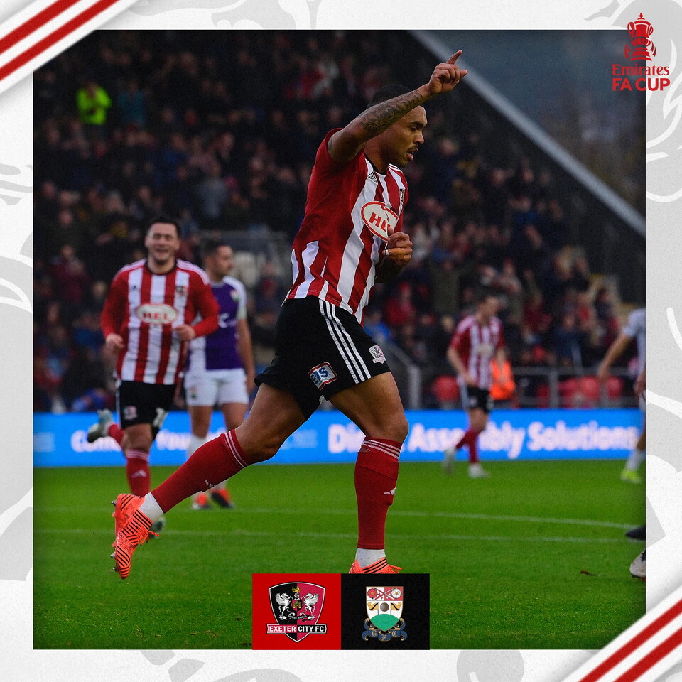 Josh Magennis, in his red and white home shirt, celebrating the opening goal. He has one arm raised in the air, pointing to the sky.