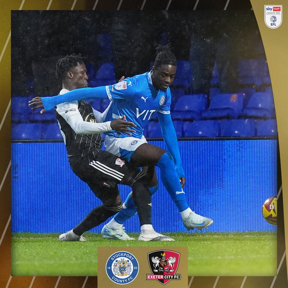 Vincent Harper, in his black third shirt, lunging in for a tackle against a blue stockport man.